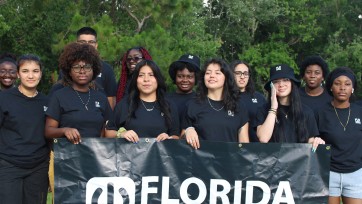 12 people in black T-shirts stand behind banner for Florida Student Power.